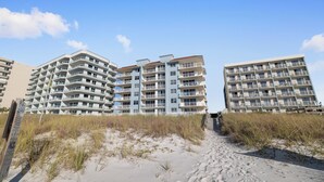 Un hôtel situé en bord de mer, doté de nombreux balcons, avec une plage de sable fin juste devant et un ciel dégagé.