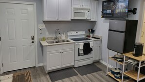 Una cocina moderna con muebles blancos, microondas integrado, pileta de acero inoxidable y refrigerador negro.