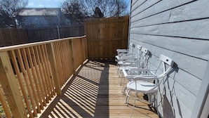 Una terraza de madera con un tapete de bienvenida, sillas blancas y una valla de madera.