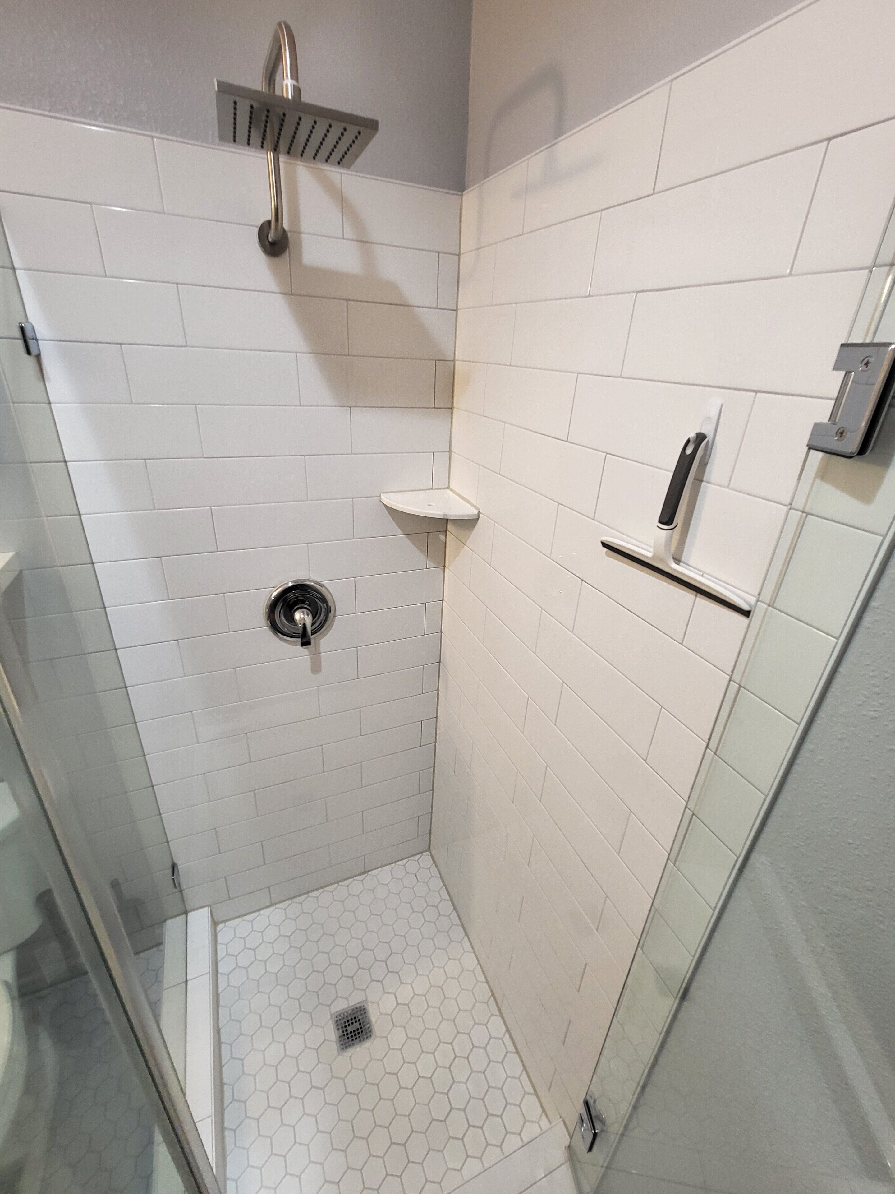A small, enclosed shower area with white tiles, a glass door, and a metal showerhead.