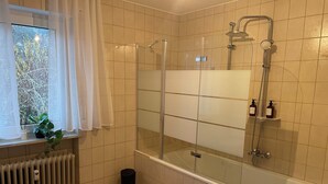 Une salle de bain moderne avec une douche à parois de verre, une baignoire et une fenêtre donnant sur les arbres.