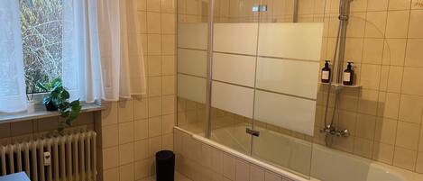 A modern bathroom with a glass-enclosed shower, a bathtub, and a window with a view of trees.