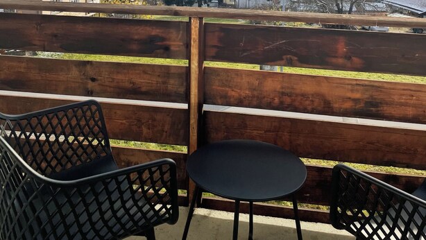 Un balcon avec deux chaises et une table, donnant sur un paysage montagneux parsemé de maisons et d’une église.