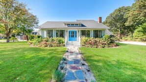 A two-story house with a blue front door, a covered porch, and a stone pathway leading to the entrance. - Relaxing Cape Cod Stay in a Charming Osterville Setting RPAM121 (Osterville)