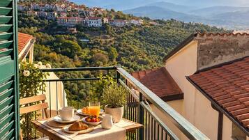 Ein Balkon mit Frühstückstisch, mit Blick auf ein Hügeldorf und Berge.