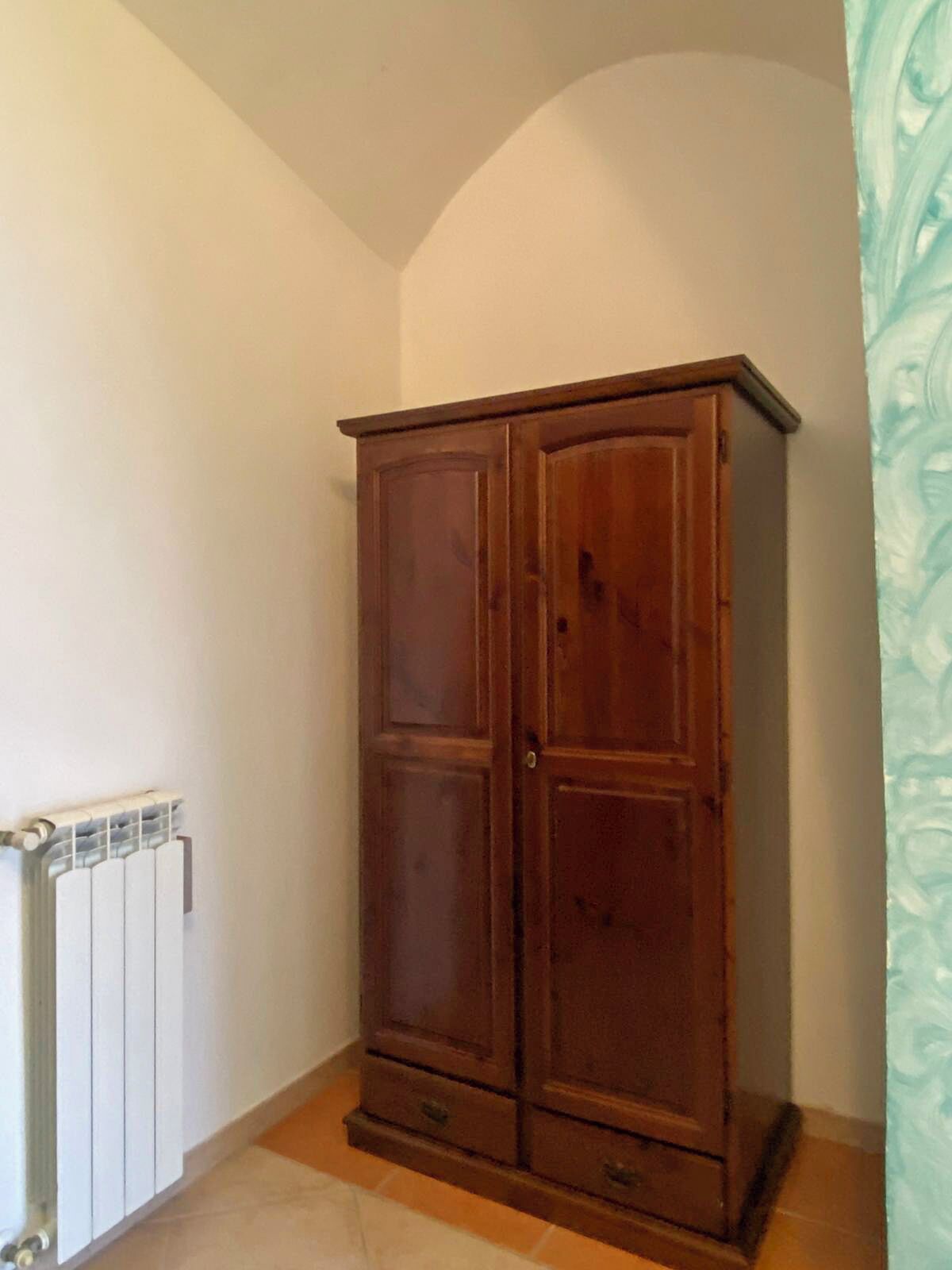 Une chambre d’angle avec une armoire en bois, un radiateur et un sol carrelé.