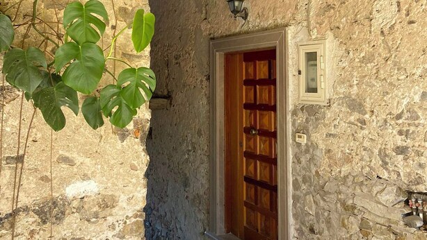 Un estrecho pasillo de piedra con una puerta de madera, una ventana pequeña y un farol arriba.