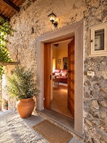 A stone facade with a wooden door leading to a room with a red sofa and a painting on the wall.