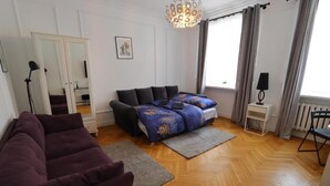 A modern living room with a sofa, a bed with patterned bedding, a standing lamp, and a window with curtains. - Fantastic Inn Warsaw - KP69 (Warsaw)