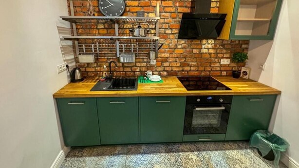 A kitchen with green cabinets, a wooden countertop, a brick wall, a black range hood, and a clock. - Fantastic Inn Warsaw - KP69 (Warsaw)