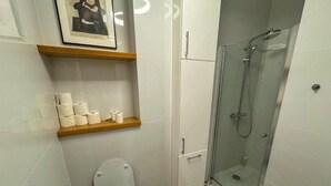 A bathroom with a toilet, a shower, and a shelf with toilet paper. - Fantastic Inn Warsaw - KP69 (Warsaw)