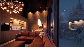 A modern interior with a large leather sofa, a kitchen area, and a view of a snowy forest.