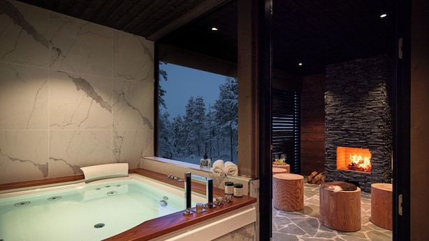 A modern bathroom with a marble wall, a large bathtub, and a stone fireplace.