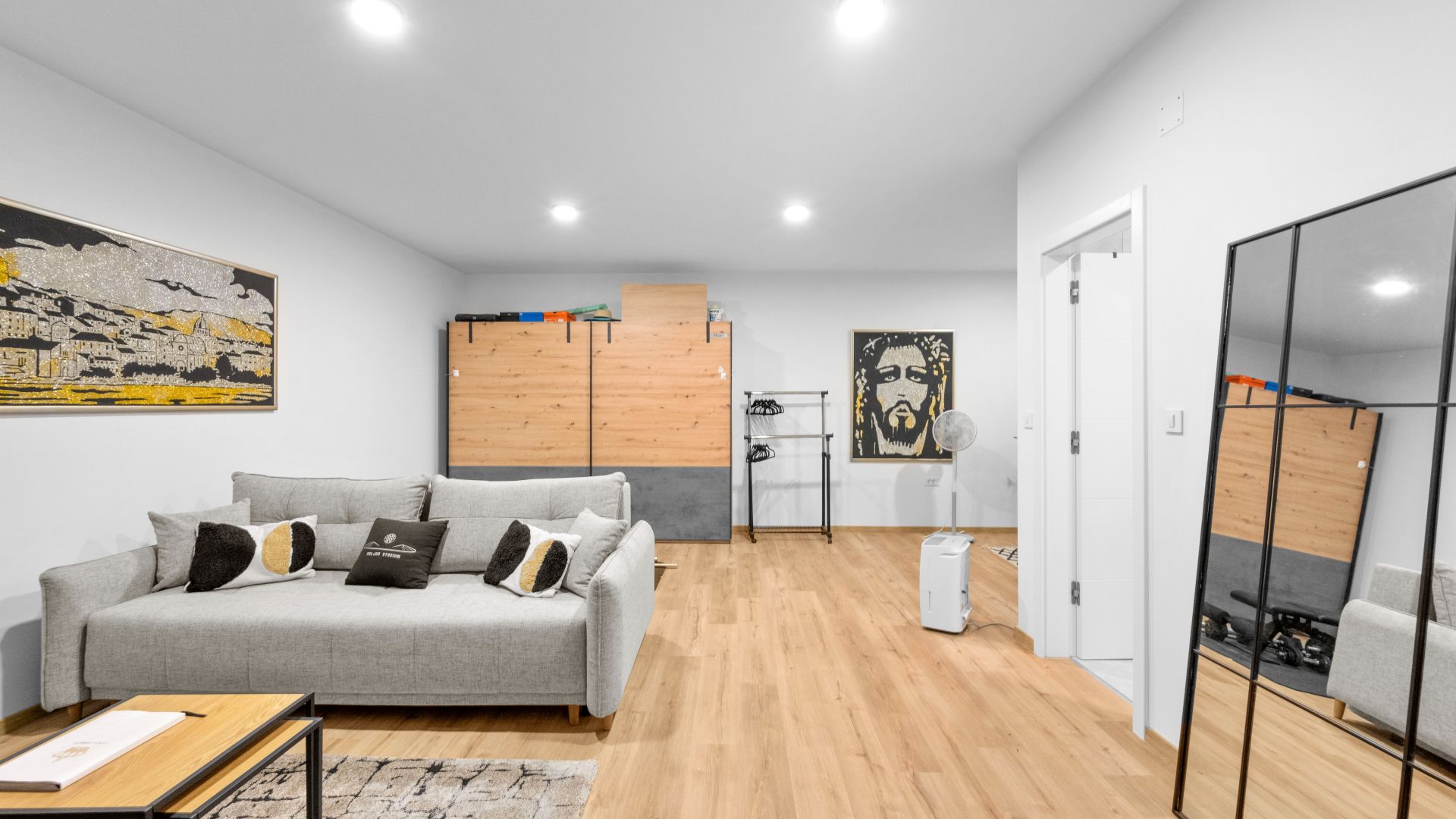 A modern living room with a grey sofa, wooden flooring, and a cityscape painting.