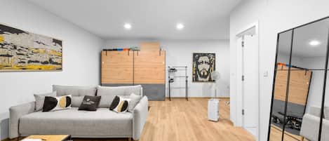 A modern living room with a grey sofa, wooden flooring, and a cityscape painting.