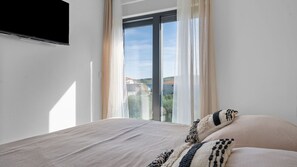 A bedroom with a bed, a TV mounted on the wall, and a window with curtains. - Boho Beach House by Villas Guide (Vodice)