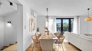 Een moderne eetruimte met een lange tafel, rieten stoelen en hanglampen.