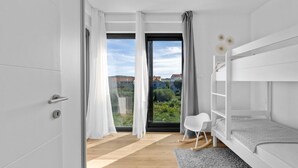 Een moderne slaapkamer met een stapelbed, uitzicht op groen en gebouwen, en een groot raam met gordijnen.