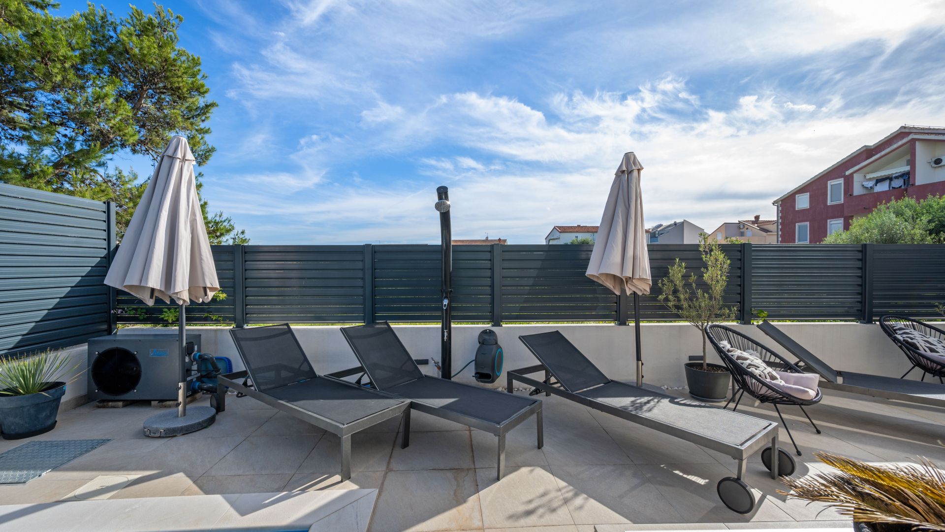 An outdoor patio with lounge chairs, umbrellas, and a small tree.