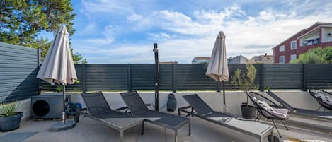 An outdoor patio with lounge chairs, umbrellas, and a small tree.