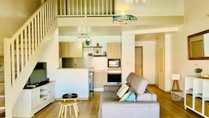 Un apartamento moderno con una escalera, una cocina con armarios de madera, un sofá gris y un taburete pequeño de madera.