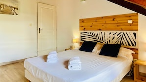 Una cama bien hecha con dos toallas, un cabecero de madera con diseño de hojas, una puerta blanca y una mesita de noche con una lámpara.