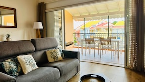 Un salón con un sofá gris, una mesita con una lámpara y vistas a un balcón con mobiliario exterior.