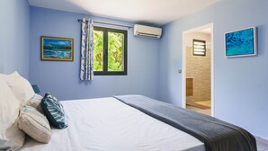 Ein Schlafzimmer mit einem Bett, Kissen, einem Fenster mit Vorhängen und zwei Bildern an der Wand.