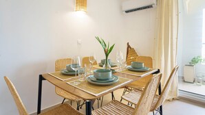 Ein Essbereich mit Tisch für vier Personen, Korbstühle, einer gewobenen Leuchte und Blick durch eine Glastür.