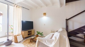 Ein Wohnzimmer mit einer Couch, einem Fernseher, einer Holzkommode, einer Pflanze und einer Treppe.