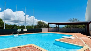 Una piscina con un borde empedrado, una zona de estar cubierta y vistas al cielo y nubes.