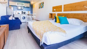Quarto de hotel moderno com uma cama grande, um sofá, máquina de lavar roupa e uma pequena cozinha.