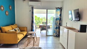 A living room with a sofa, a small table, a TV, and a balcony with a table and chairs. - Comfortable studio with terrace, cistern and pool access (Le Gosier)