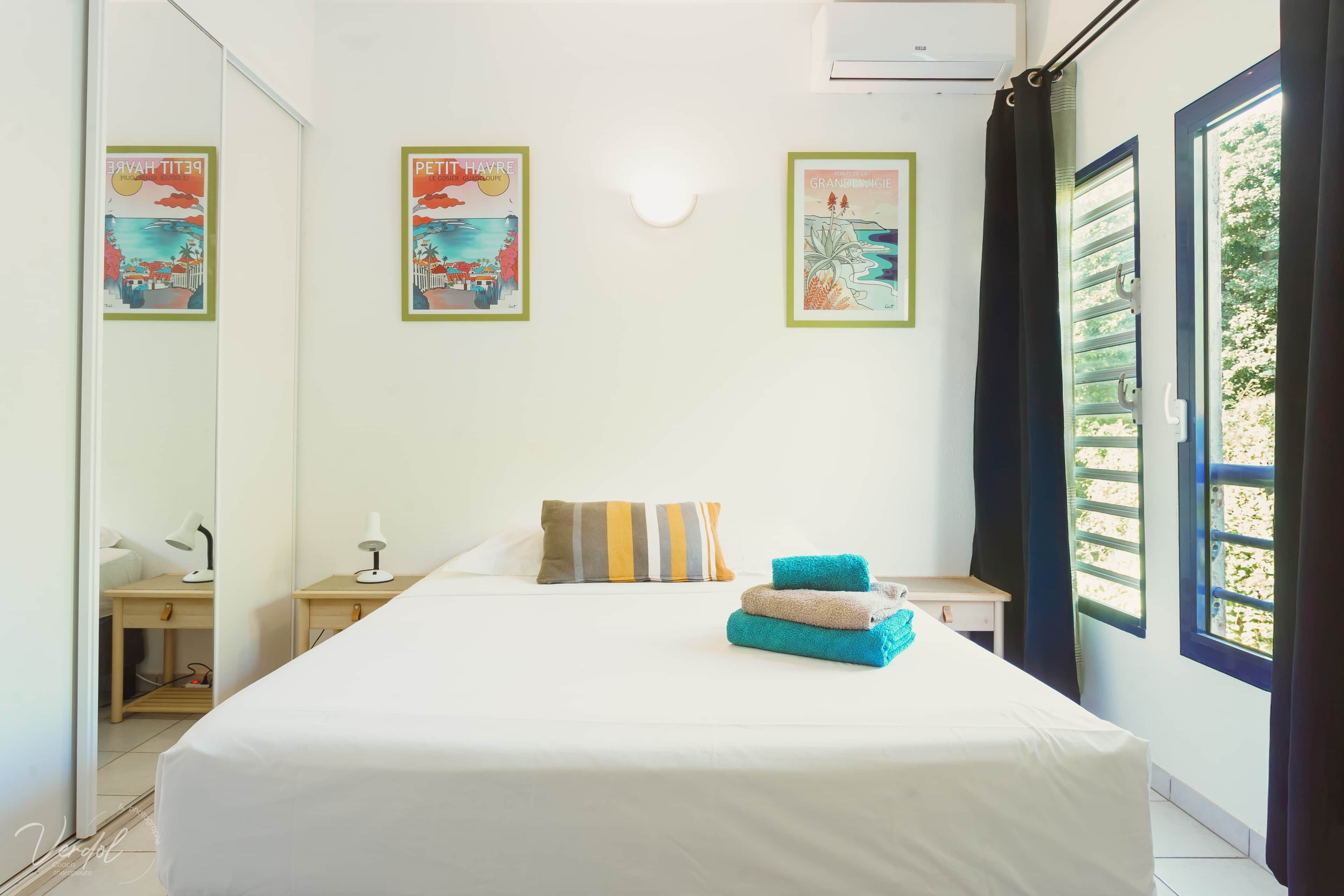 A hotel room with a large bed, two bedside tables, a nightstand, a mirror, and a window with curtains.