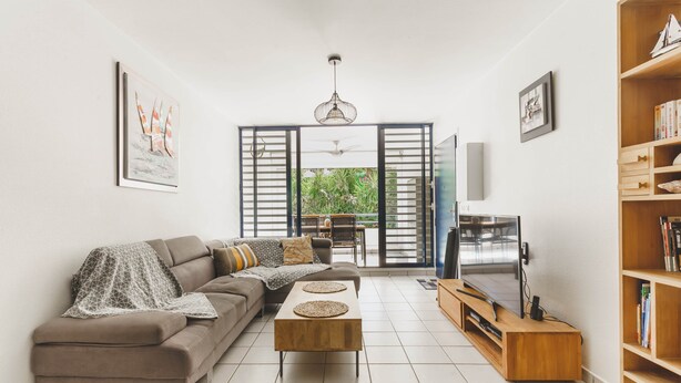 A modern living room with a sofa, coffee table, TV stand, and bookshelf. - Spacious duplex near the beach with cistern (Le Gosier)