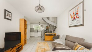 A modern living room with a flat-screen TV, wooden entertainment unit, and a staircase leading to an upper level. - Spacious duplex near the beach with cistern (Le Gosier)