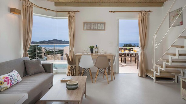 Een moderne woonkamer met een bank, eettafel en stoelen, een trap en uitzicht op zee.