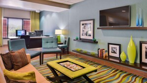 A modern hotel lobby with a sofa, armchairs, a coffee table, a desk with a computer, and a TV on the wall. - Spark By Hilton Decatur (Decatur)