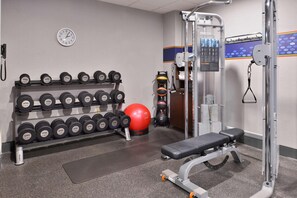 A gym with dumbbells, a red exercise ball, a bench, and a wall clock. - Spark By Hilton Decatur (Decatur)