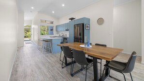 A modern kitchen with blue cabinets, a wooden dining table, and black chairs. - Bluwren: 4  BR, 2.5  BA House in South west rocks, Sleeps 6 (South west rocks)