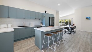 A modern kitchen with grey cabinets, a white countertop, and a central island with stools. - Bluwren: 4  BR, 2.5  BA House in South west rocks, Sleeps 6 (South west rocks)