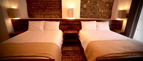 A hotel room with two beds, a brick floor, stone wall decor, and wall-mounted lamps.