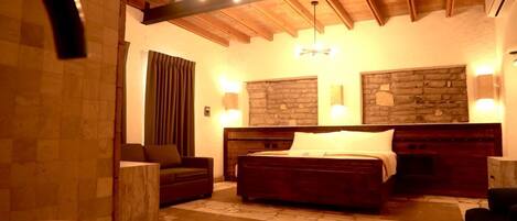 Un dormitorio amplio con una cama grande, techo de madera, paredes de piedra y una bañera.