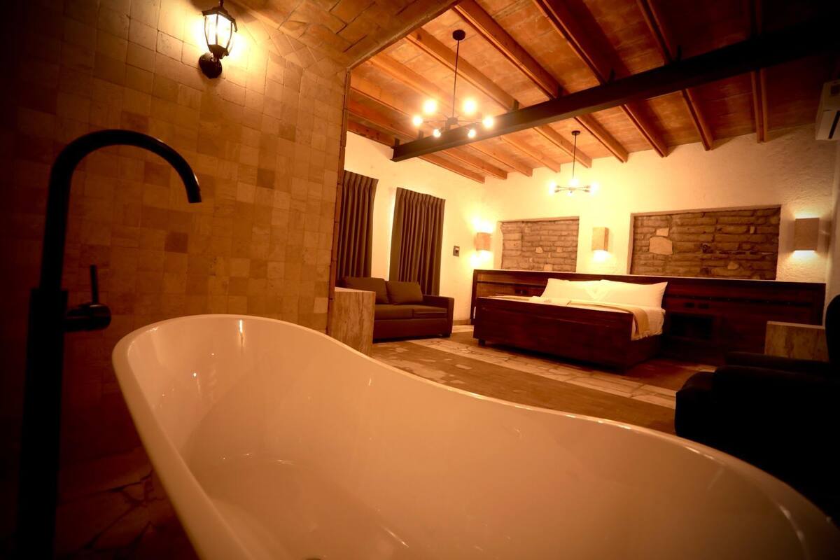 Ein Zimmer mit einer großen Badewanne, Holzbalkendecke, einem Bett mit Kopfteil und einer Steinwand.