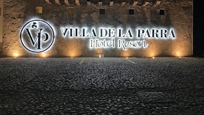 A sign for Villa de la Parra Hotel Resort with a stone wall background and illuminated lettering. - Hotel Villa de la Parra (Parras de la Fuente)