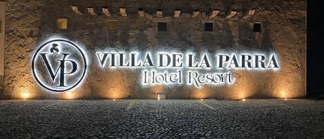 Naamplaatje voor Hotel Resort Villa de la Parra, met een stenen muur als achtergrond en verlichte letters.