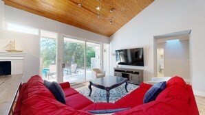 Un soggiorno con un divano rosso, un soffitto in legno, una televisione a schermo piatto e una porta vetrata che dà sull'esterno.