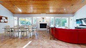 Un ampio soggiorno con soffitto in legno, un camino, un divano rosso, un'area pranzo con sedie e una TV a parete.