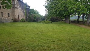 A castle courtyard with a grassy lawn, stone walls, and mature trees. - Schloss Burgscheidungen – Gästehaus (Laucha an der Unstrut)