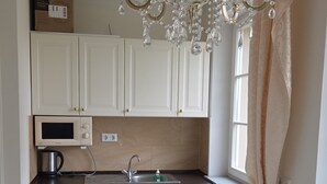 A kitchen with white cabinets, a marble countertop, a built-in microwave, a sink, and a chandelier. - Schloss Burgscheidungen – Gästehaus (Laucha an der Unstrut)